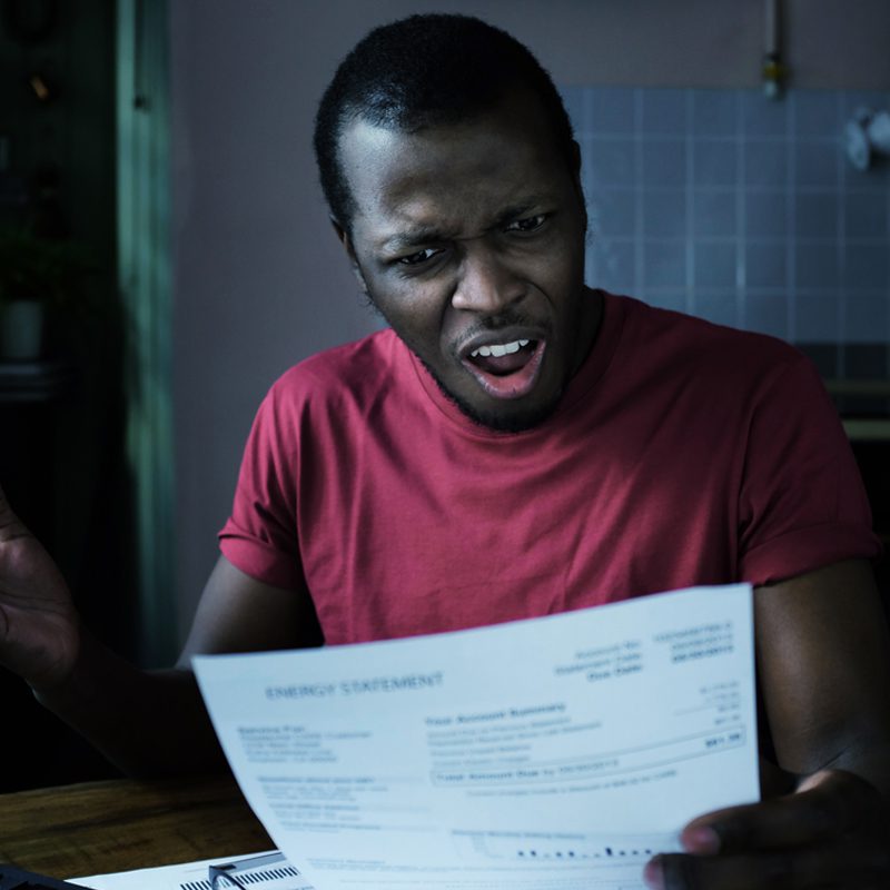 Young frustrated african american man looks at bill, worried about troubles with payments